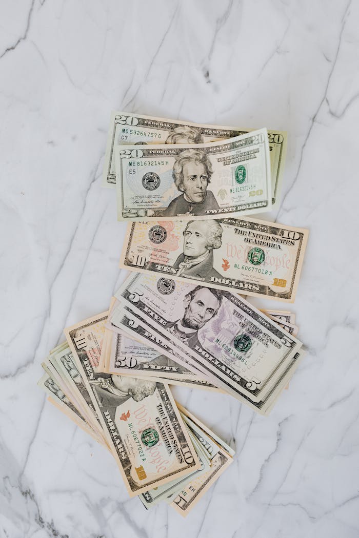A collection of various US dollar bills laid out on a marble background.